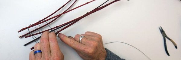 Hände arbeiten mit Zweigen an Drahtskulpturen aus Draht und Naturmaterial